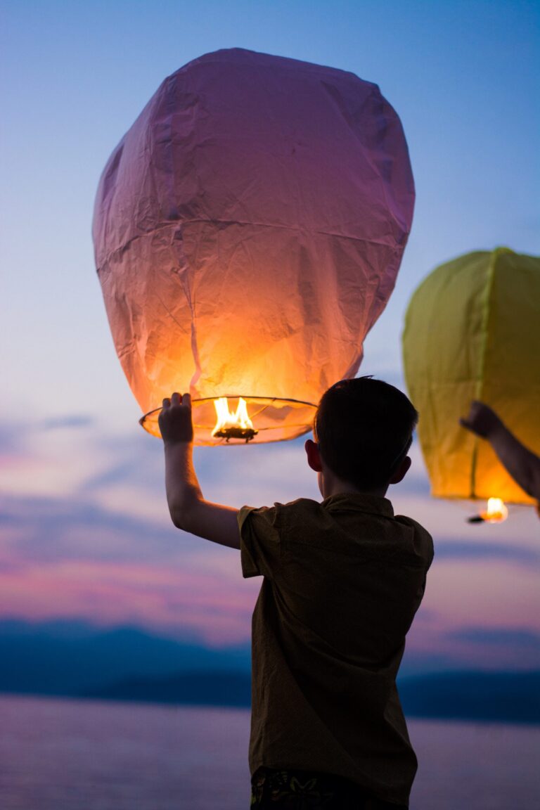A boy releasing a glowing paper sky lantern at dusk