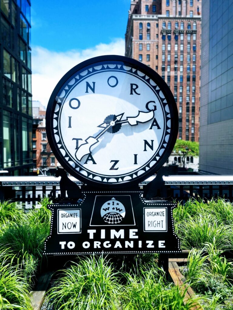 Outdoor clock sculpture with signs reading ‘Time to Organize,’ ‘Organize Now,’ and ‘Organize Right’