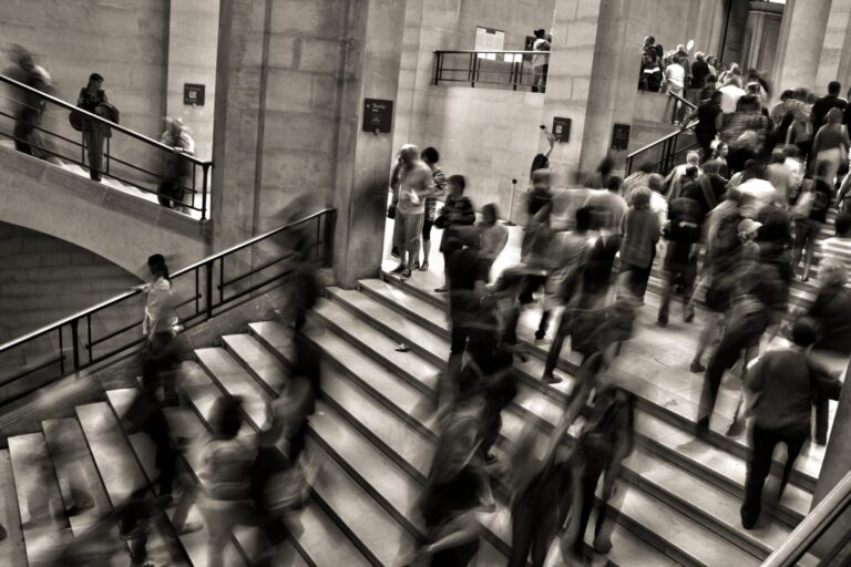Black-and-white photo of a crowded stairwell with motion-blurred people moving in different directions