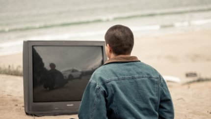 man meditating on beach in front of an unplugged tv