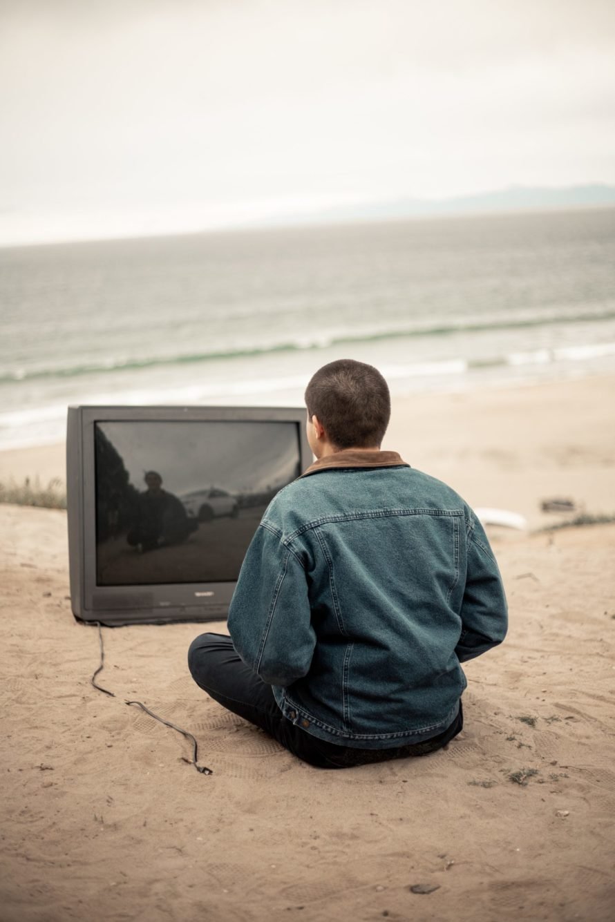 man meditating on beach in front of an unplugged tv