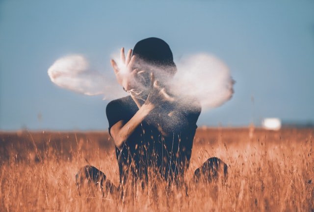 Man in Lotus Position in a field waving clouds around his head.