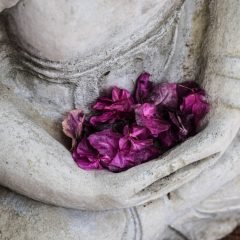 Concrete statue in meditation position holding purple flowers