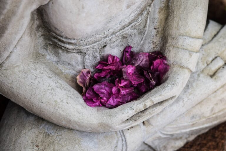 Meditating statue holding purple flowers during a quiet forgiveness practice