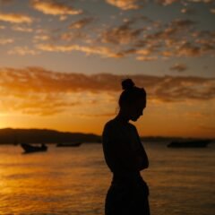 sad woman standing on coast of sea at sunset