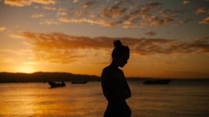 sad woman standing on coast of sea at sunset