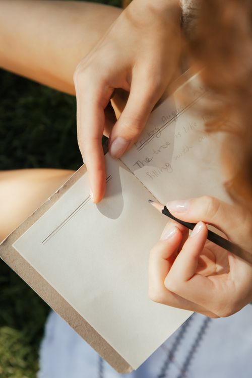 Close-up of a woman writing in a journal outdoors, photographed by Ron Lach on Pexels